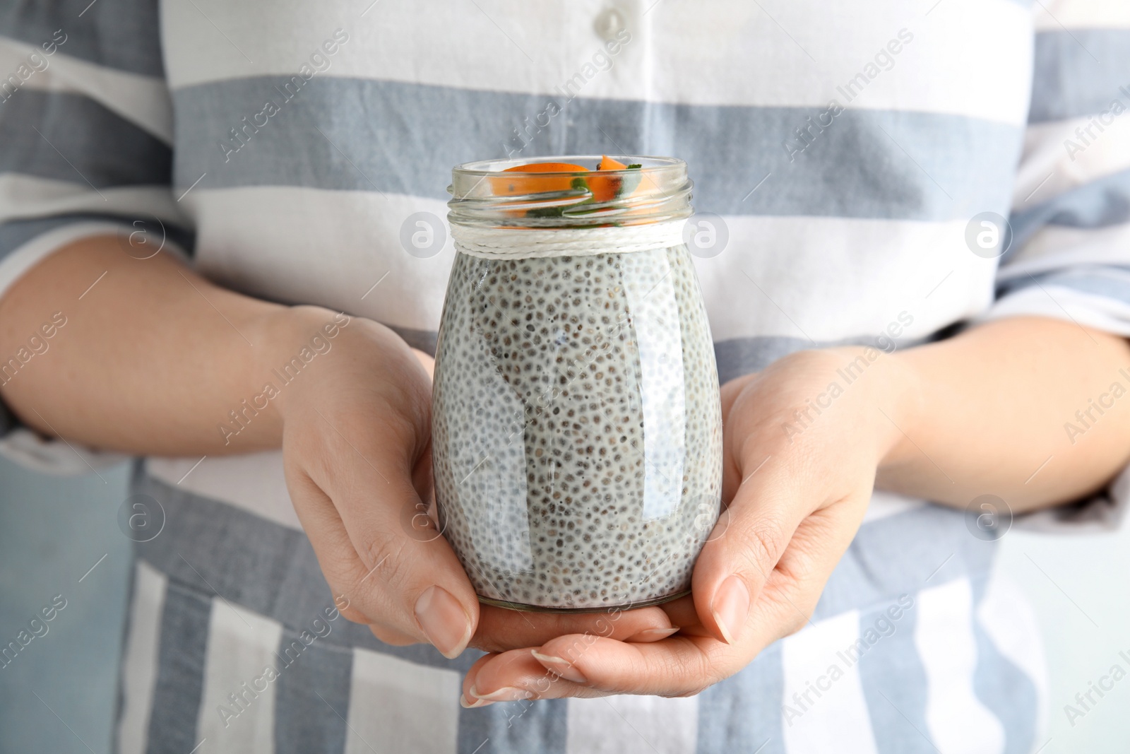 Photo of Young woman holding jar of tasty chia seed pudding with persimmon, closeup