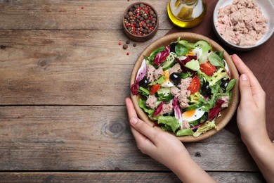 Photo of Woman holding bowl of delicious salad with canned tuna at wooden table, top view. Space for text