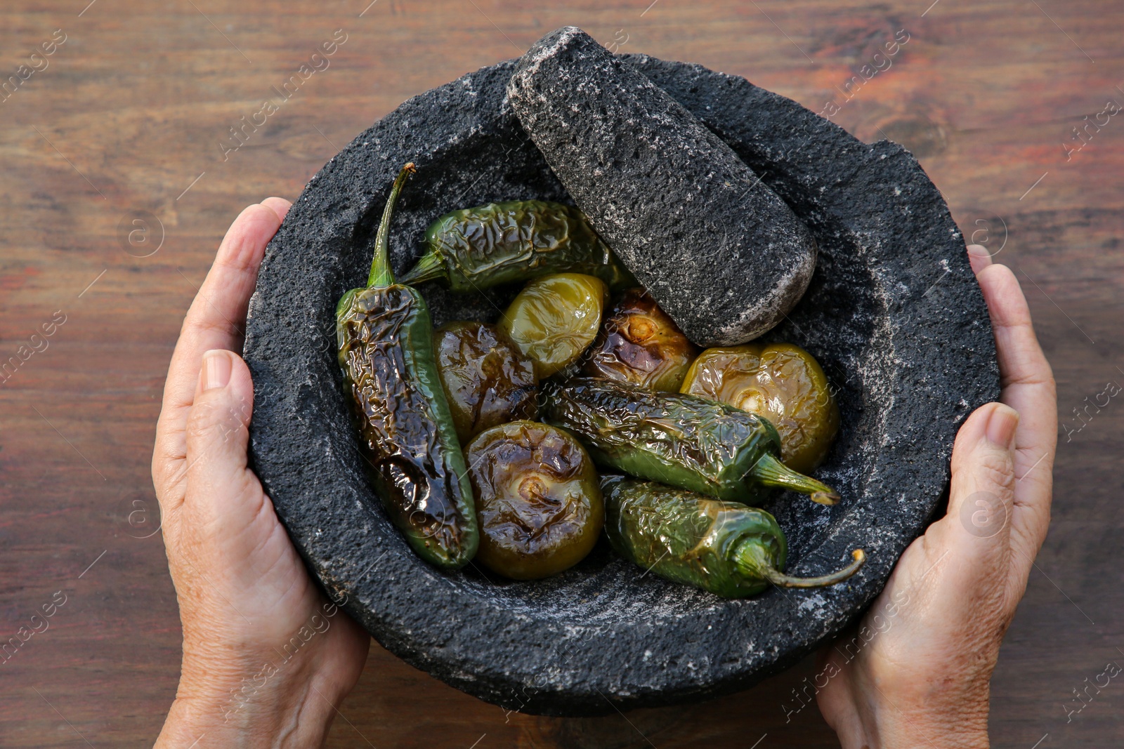 Photo of Woman holding mortar with ingredients for salsa sauce at wooden table, above view