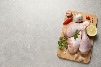 Photo of Wooden board with fresh raw chicken legs and other products on light grey table, top view. Space for text