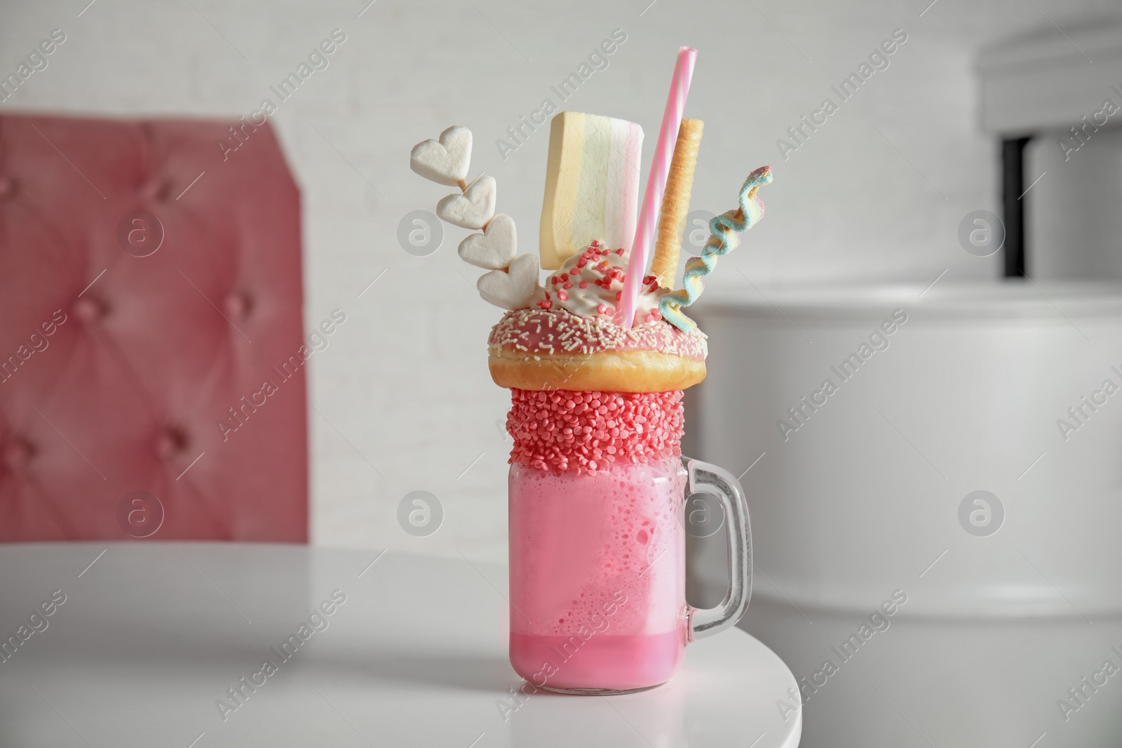 Photo of Tasty milk shake with sweets in mason jar on table at cafe