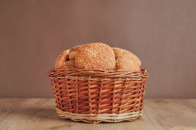 Photo of Wicker basket of fresh buns with sesame seeds on wooden table