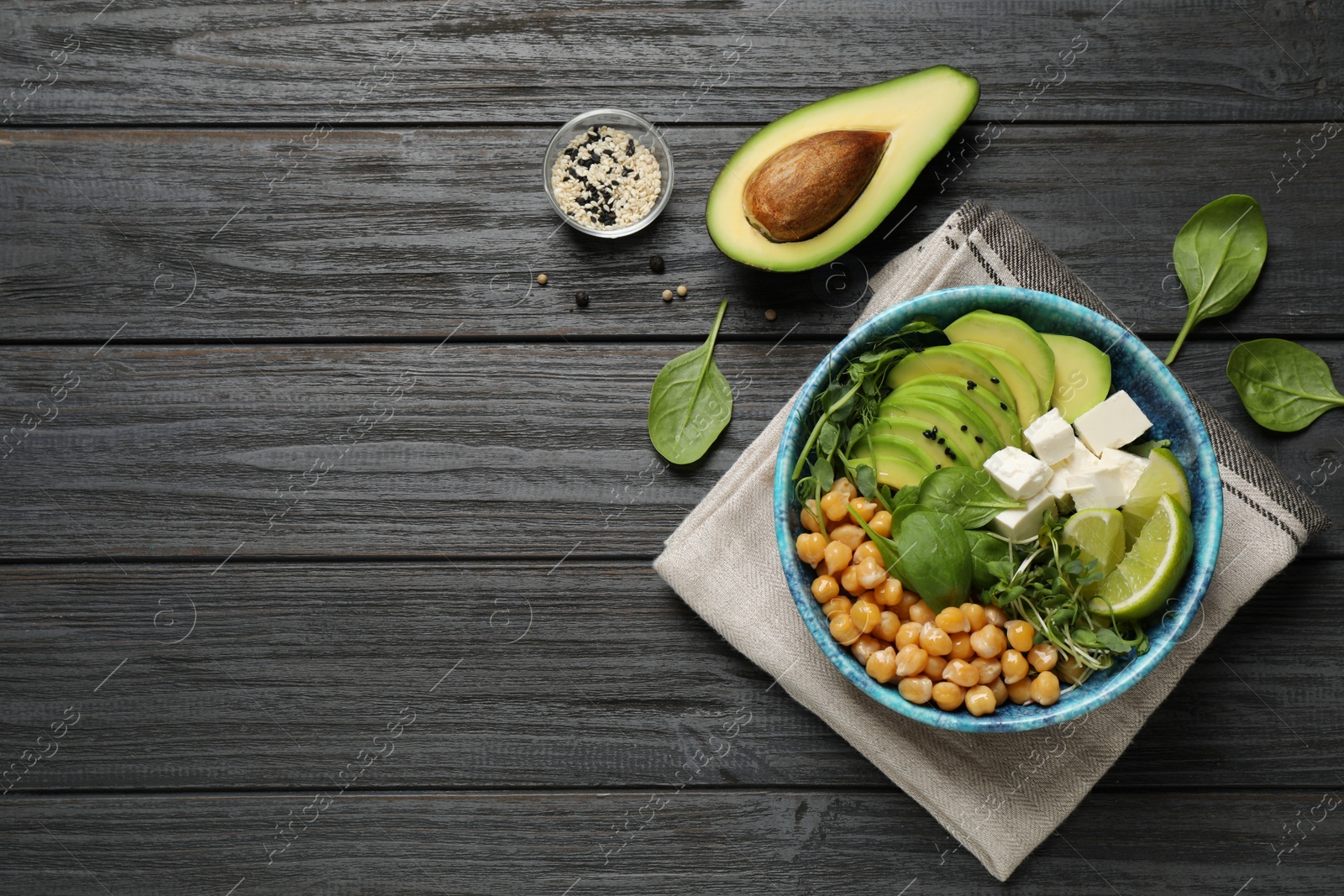 Photo of Delicious avocado salad with chickpea on black wooden table, flat lay. Space for text