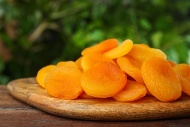 Photo of Tasty apricots on wooden table against blurred green background. Dried fruits