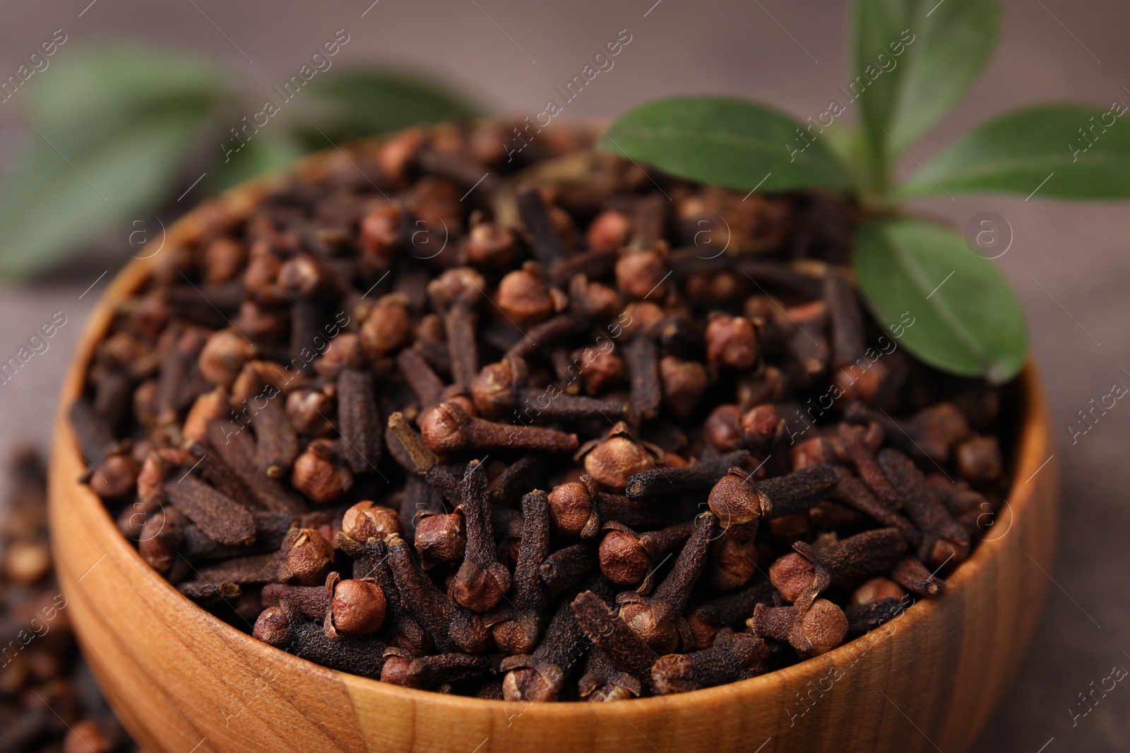 Photo of Aromatic cloves and green leaves in bowl on table, closeup