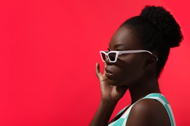 Photo of Fashionable portrait of beautiful woman with stylish sunglasses on coral background, space for text