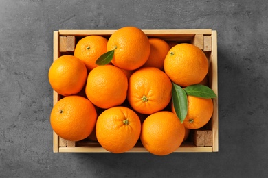 Wooden crate with ripe oranges on grey background, top view