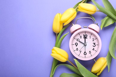 Photo of Pink alarm clock and beautiful tulips on violet background, flat lay with space for text. Spring time