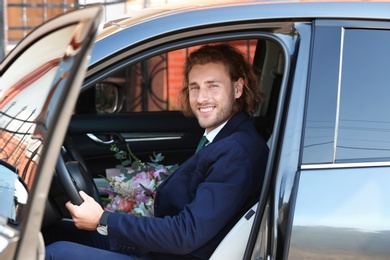 Young handsome man with beautiful flower bouquet in car