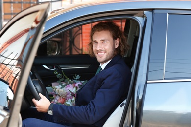 Photo of Young handsome man with beautiful flower bouquet in car