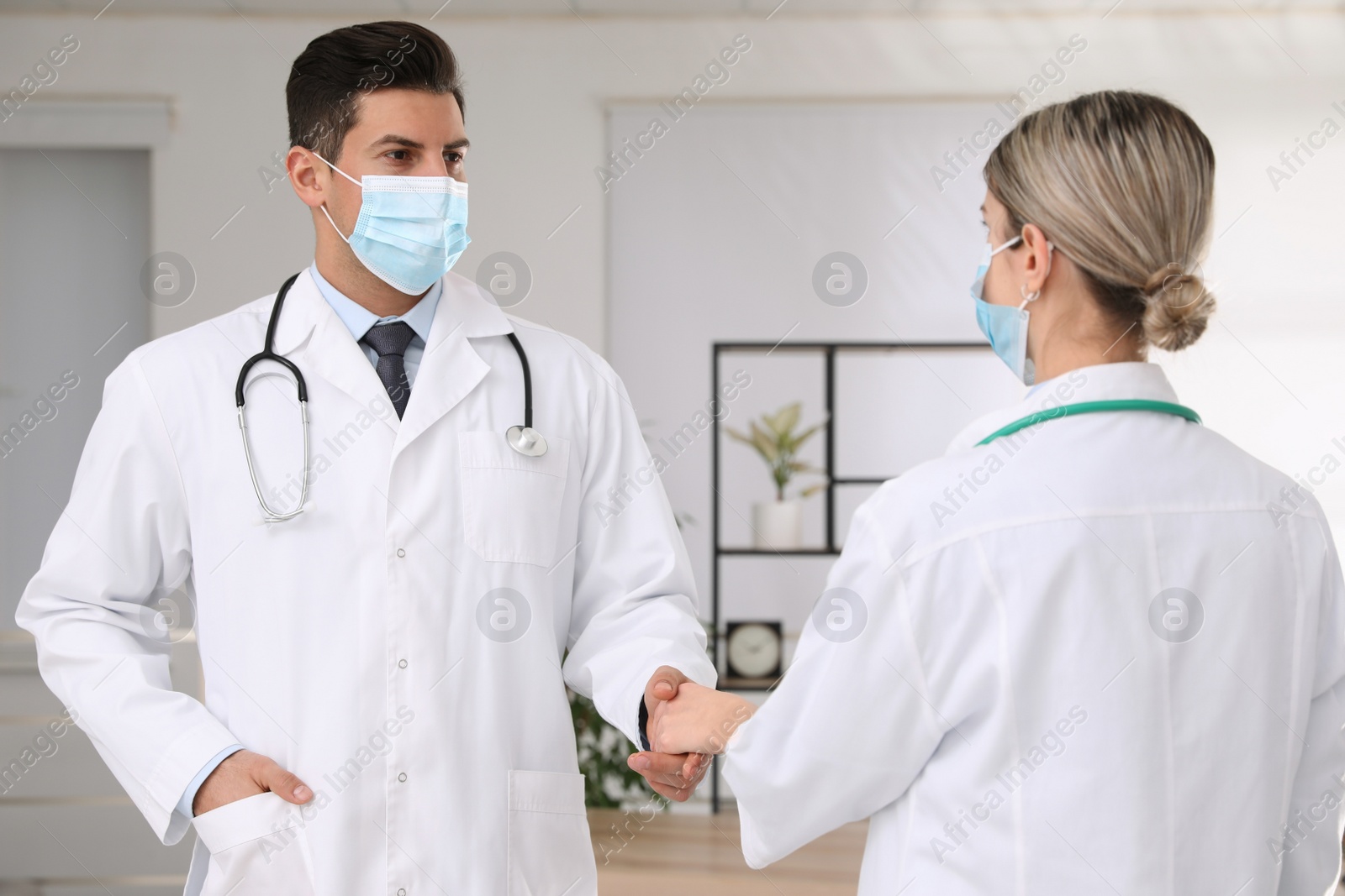 Photo of Doctors with protective masks giving handshake in clinic