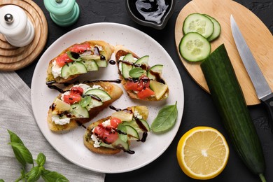 Photo of Delicious bruschettas with balsamic vinegar, toppings and products on dark textured table, flat lay