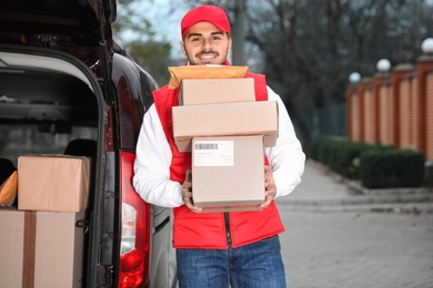 Photo of Deliveryman holding stack of parcels near van outdoors