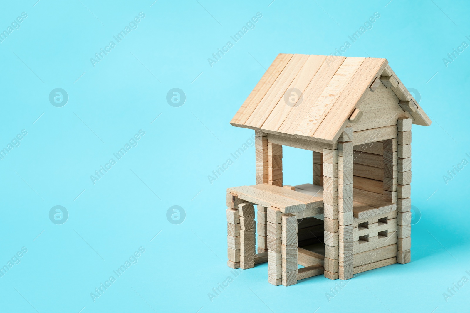 Photo of Wooden house on light blue background, space for text. Children's toy