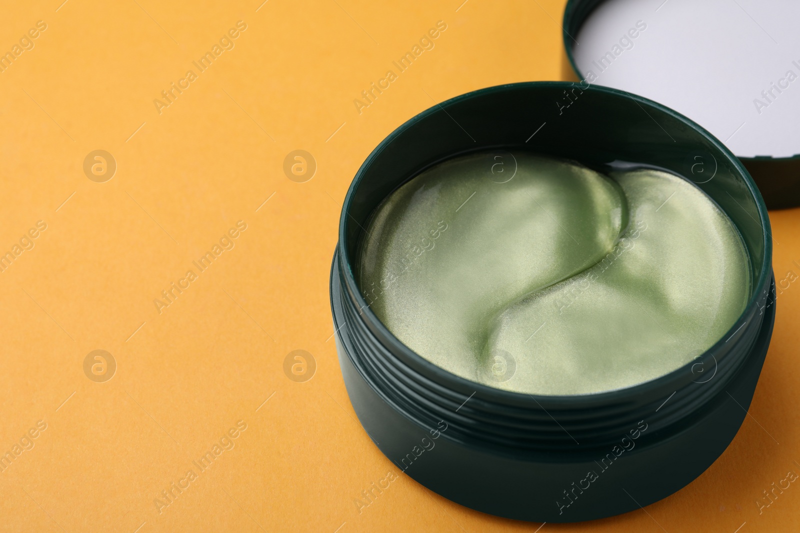 Photo of Under eye patches in jar on orange background, closeup. Space for text