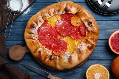 Photo of Delicious galette with citrus fruits served on blue wooden table, flat lay