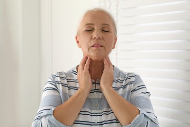 Photo of Mature woman doing thyroid self examination indoors