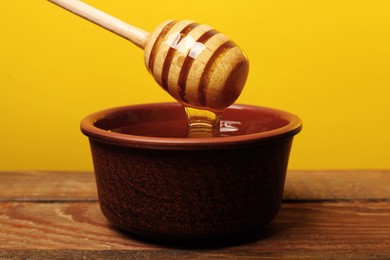 Photo of Pouring honey from dipper into bowl at wooden table against golden background