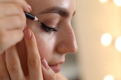Photo of Makeup product. Woman applying black eyeliner indoors, closeup