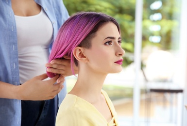 Photo of Professional hairdresser working with young woman in beauty salon. Trendy hair color