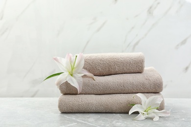 Photo of Stack of fresh towels with flowers on grey table against light background