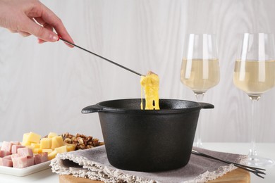 Photo of Dipping piece of ham into fondue pot with tasty melted cheese at table, closeup