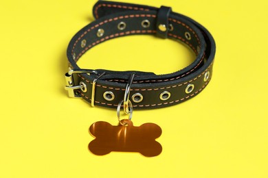 Black leather dog collar with golden tag in shape of bone on yellow background