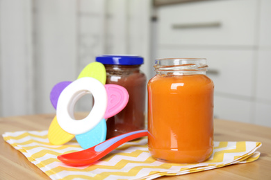 Photo of Jars with healthy baby food, spoon and toy on wooden table indoors