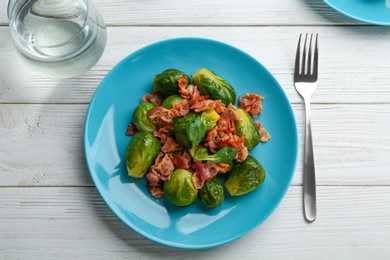 Photo of Tasty roasted Brussels sprouts with bacon on white wooden table, flat lay