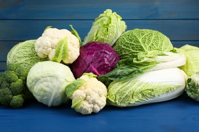 Photo of Many different fresh cabbages on blue wooden table
