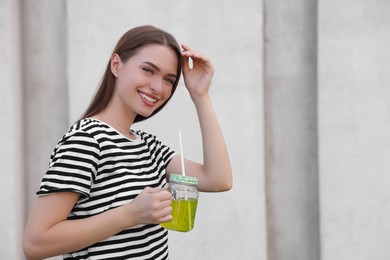 Photo of Young woman with mason jar of fresh juice outdoors, space for text