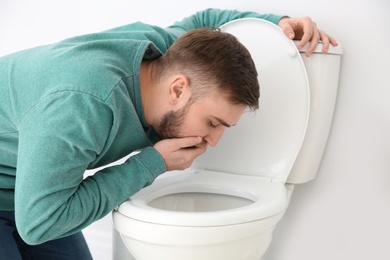 Young man suffering from nausea over toilet bowl indoors