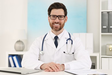 Photo of Medical consultant with glasses and stethoscope at table in clinic