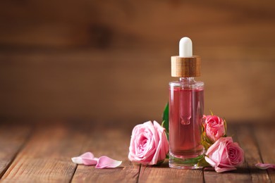 Bottle of essential rose oil and roses on wooden table. Space for text