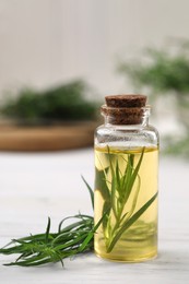 Photo of Bottle of essential oil and fresh tarragon leaves on white wooden table