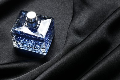 Photo of Luxury men's perfume in bottle on black satin fabric, space for text