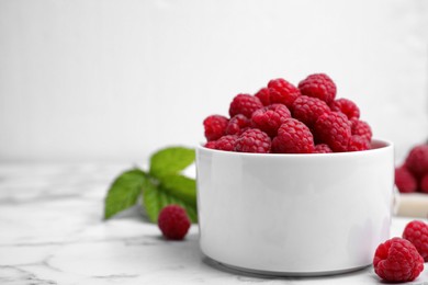 Photo of Bowl with fresh ripe raspberries on white marble table. Space for text