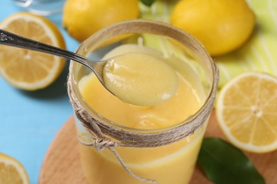 Photo of Taking delicious lemon curd from jar at light blue table, closeup