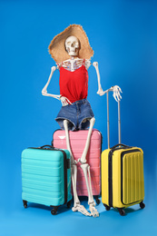 Photo of Human skeleton in summer clothes with suitcases on blue background