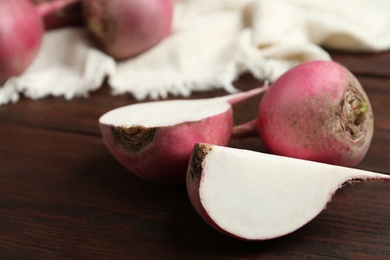 Photo of Cut and whole red turnips on wooden table, closeup