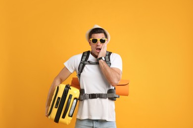 Photo of Emotional male tourist with travel backpack and suitcase on yellow background