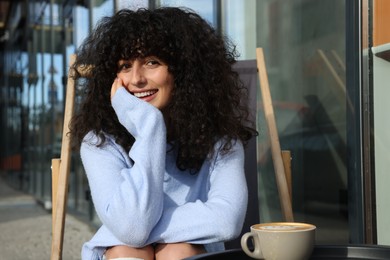 Photo of Happy young woman in stylish light blue sweater with cup of coffee at table outdoors