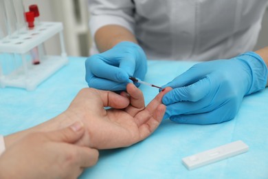 Photo of Doctor taking blood sample from patient's finger at table in clinic, closeup