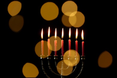 Photo of Golden menorah with burning candles against dark background and blurred festive lights