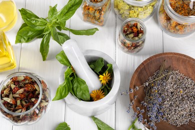 Photo of Mortar with pestle and many different medicinal herbs on white wooden table, above view