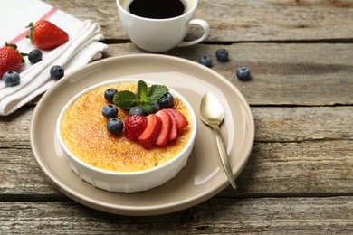 Photo of Delicious creme brulee with berries and mint in bowl on wooden table. Space for text