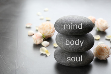 Photo of Stones with words MIND, BODY, SOUL and rose flowers on grey background, space for text. Zen lifestyle