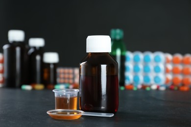 Photo of Bottle of cough syrup, dosing spoon and measuring cup on black table