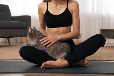 Photo of Woman stroking her cat while practicing yoga at home, closeup