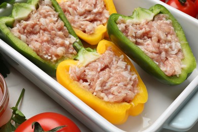 Photo of Raw stuffed peppers and ingredients on white table, closeup